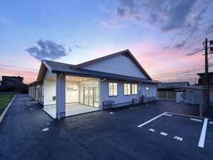 夕焼けを背景にした介護施設の建物外観。駐車場と玄関が見える